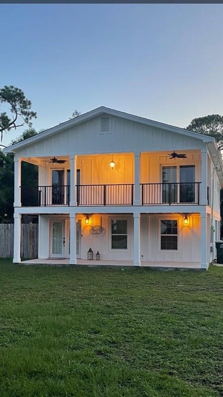 Two-story white house with covered balconies and black railings; lit windows at dusk.
