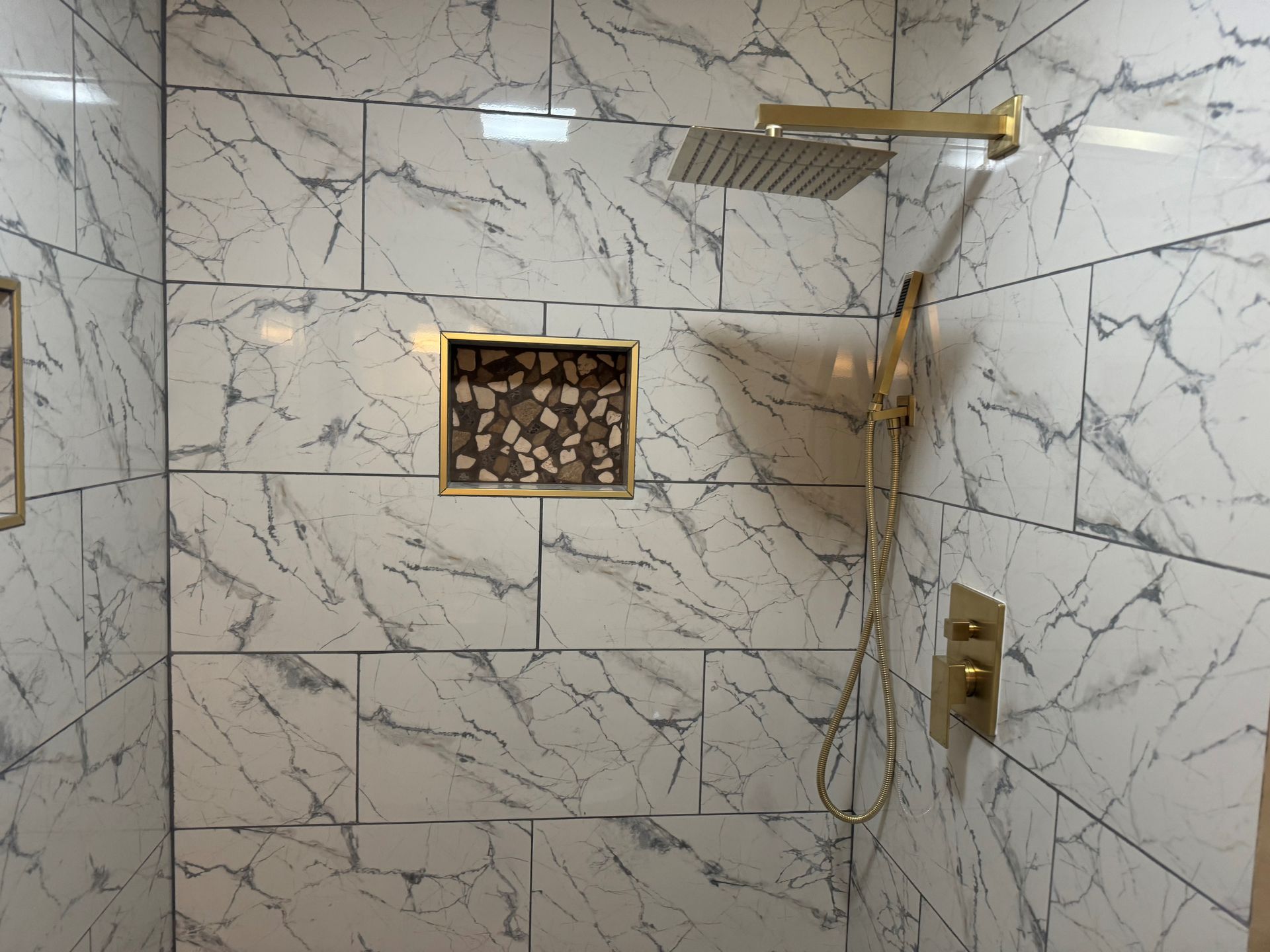 Marble-tiled shower with gold fixtures, built-in shelf with stone accents.
