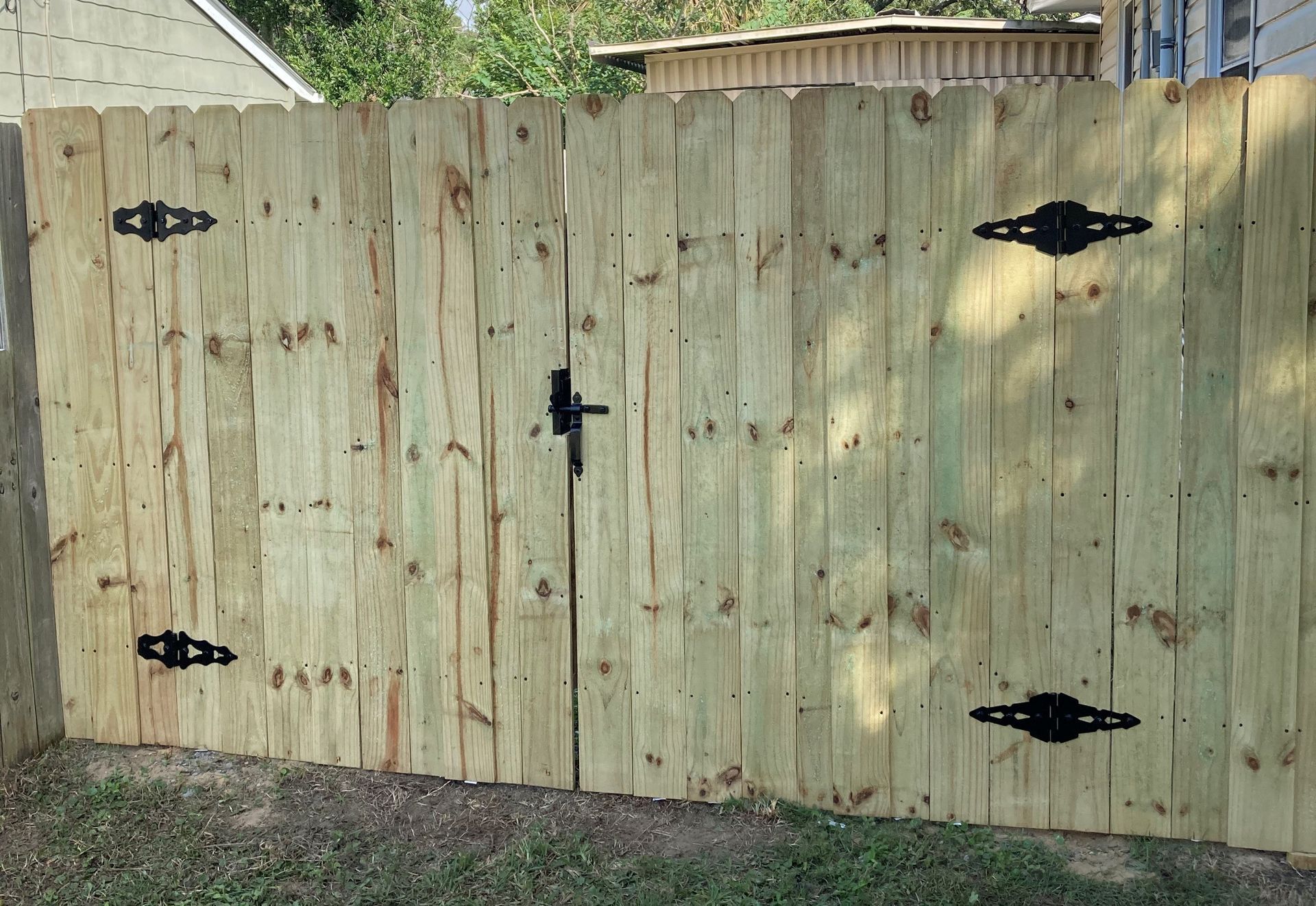 Wooden double gate, green wood, black hardware, leading into a yard.