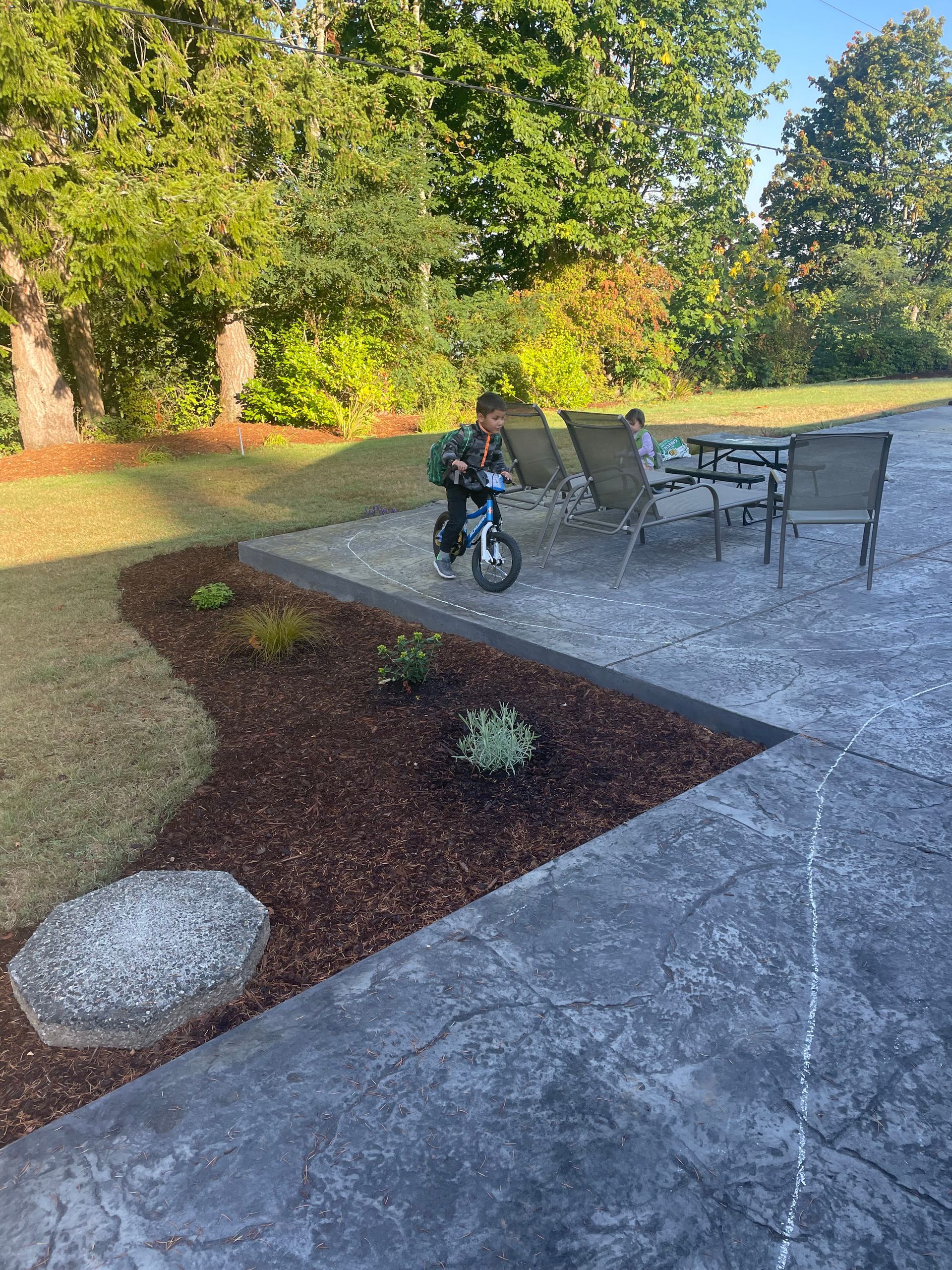 A boy is riding a bike on a patio next to a table and chairs.
