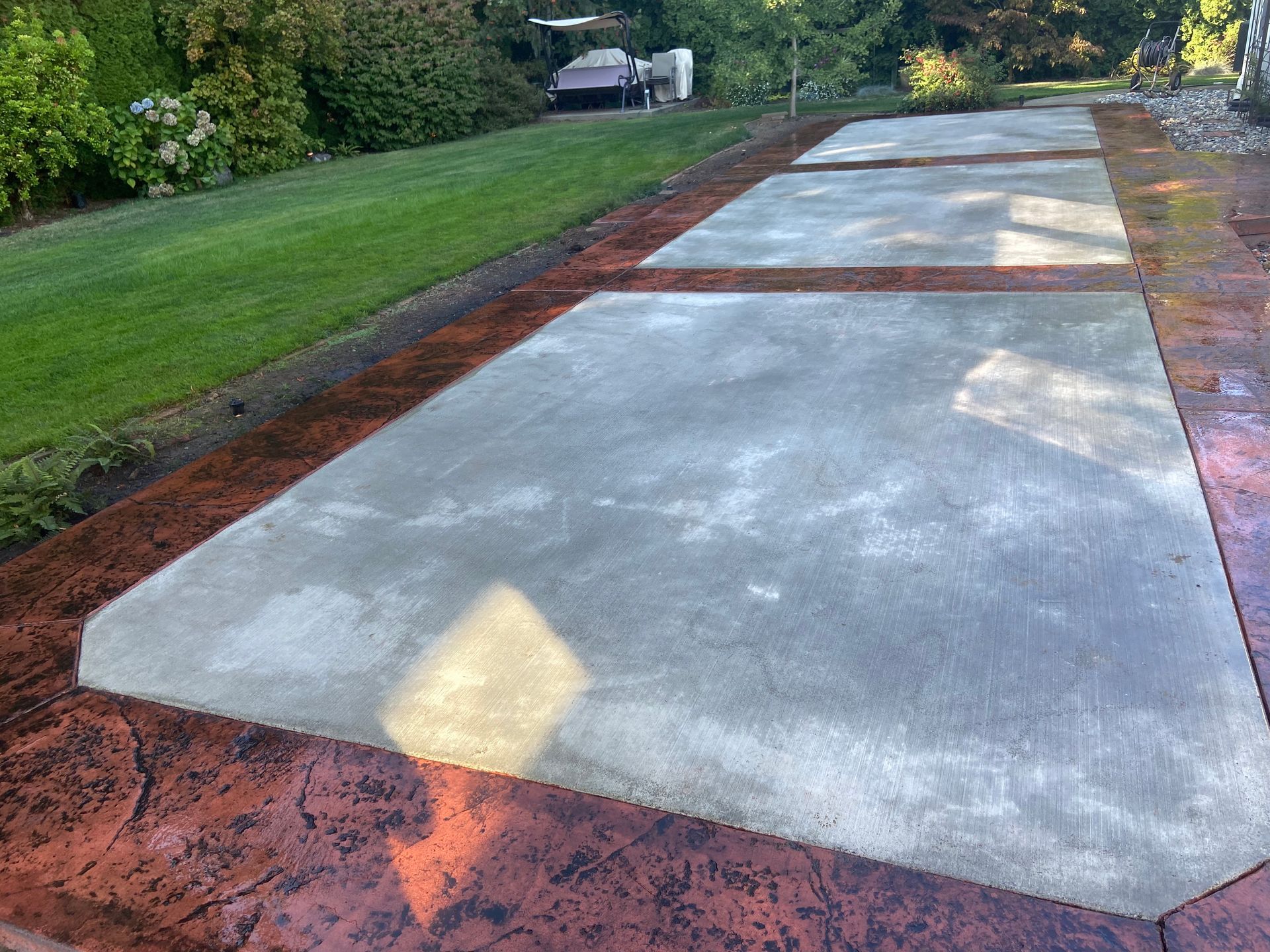 A concrete driveway with a red border and a lawn in the background.