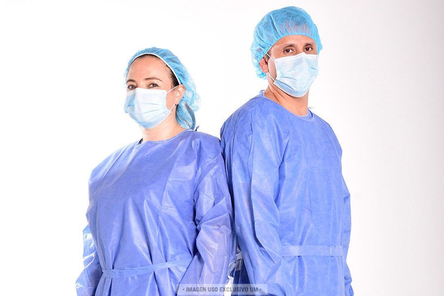 Dos personas con batas quirúrgicas azules, gorros y mascarillas, de pie espalda con espalda contra un fondo blanco.