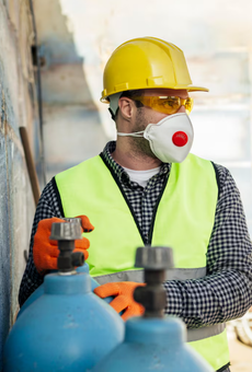 Trabajador de la construcción con equipo de seguridad: casco, respirador, guantes, chaleco, junto a cilindros de gas azules.