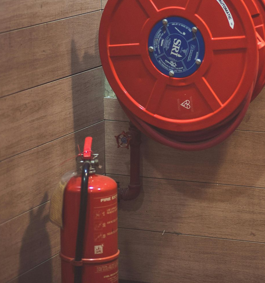 Extintor rojo junto a un carrete de manguera contra incendios montado en la pared sobre paneles de madera.