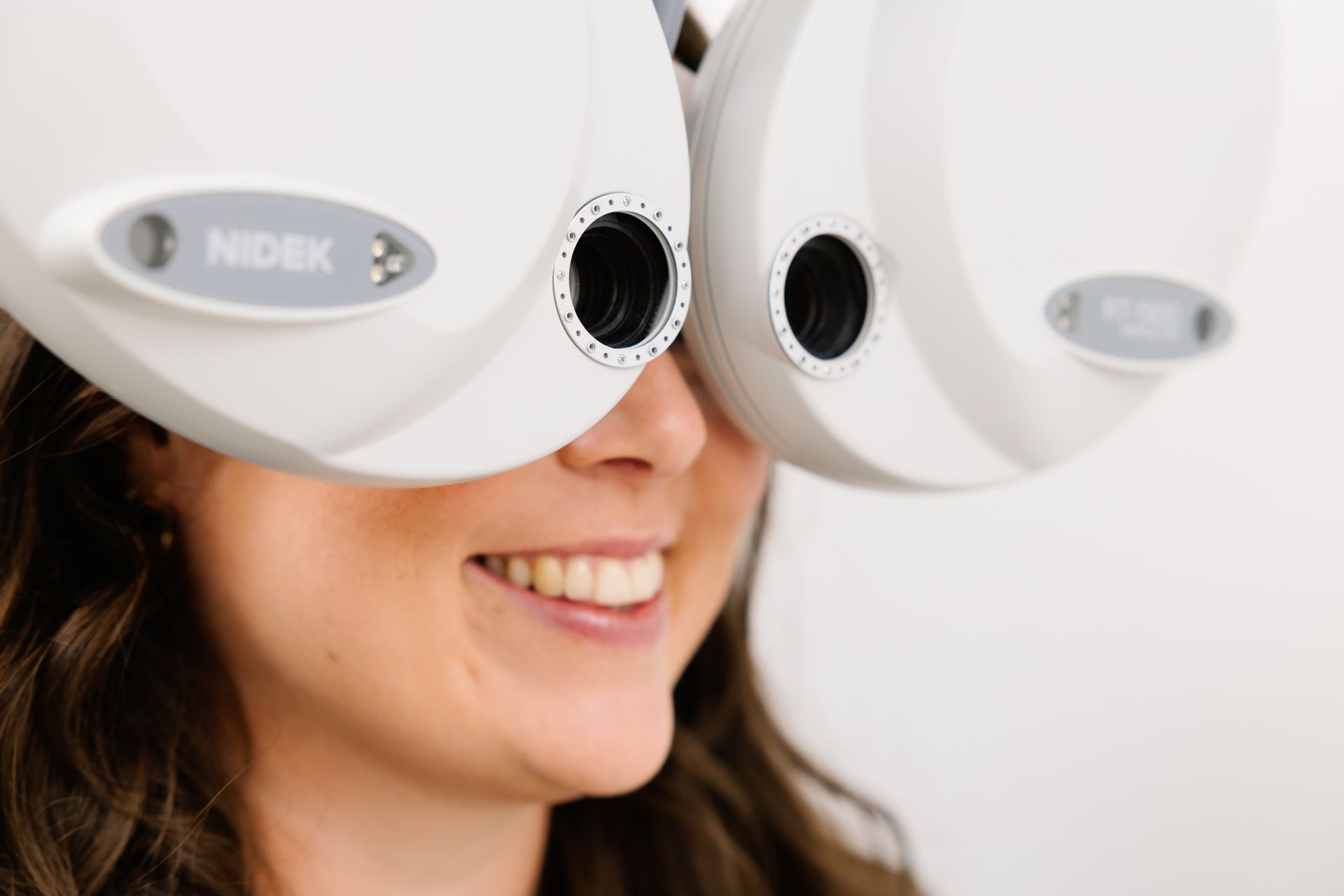 Eine lächelnde Person schaut während eines Sehtests durch ein optisches Untersuchungsgerät von NIDEK.