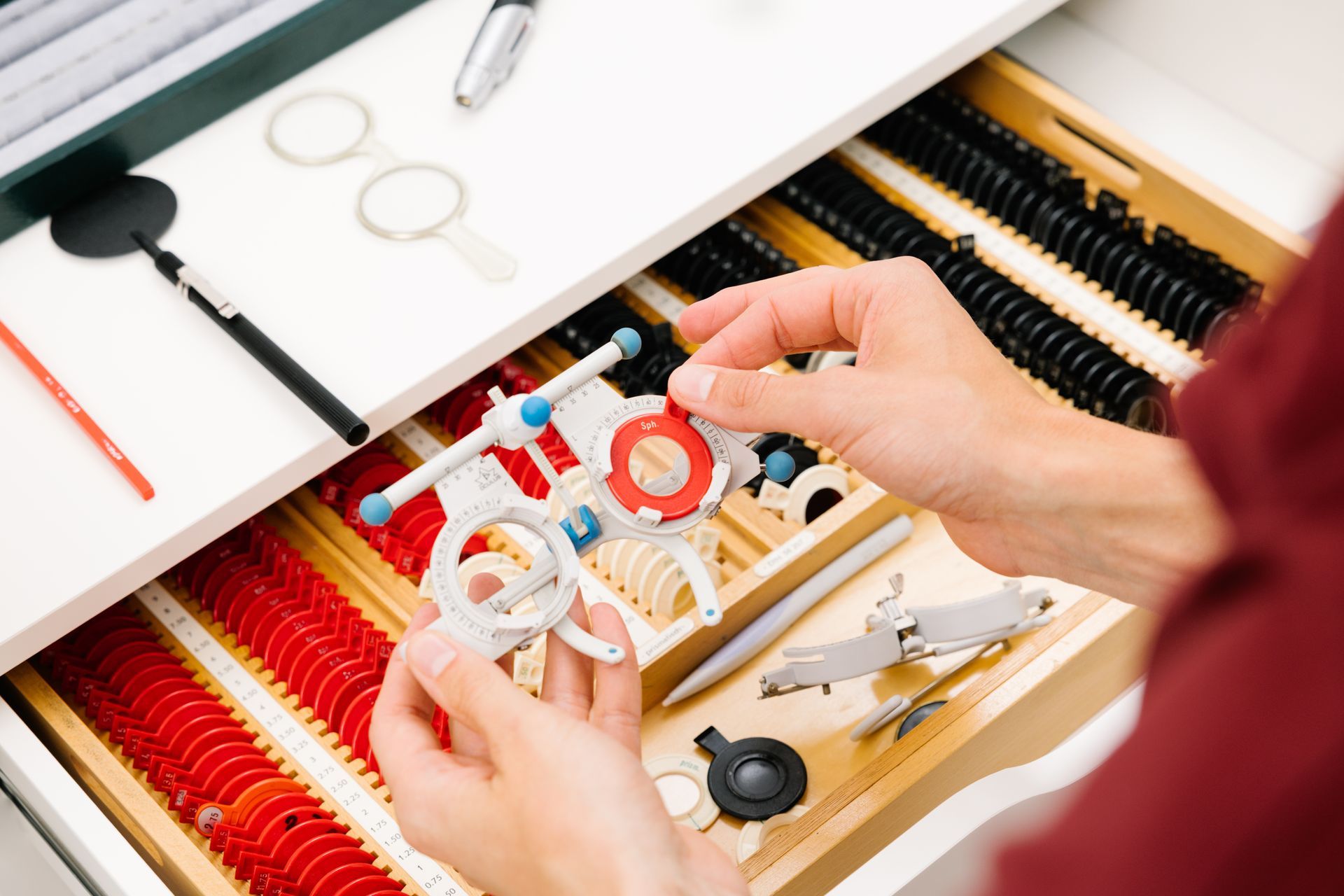 Eine Person hält in einer Augenklinik einen Proberahmen über eine Schublade voller Probelinsen für die Augenoptik.