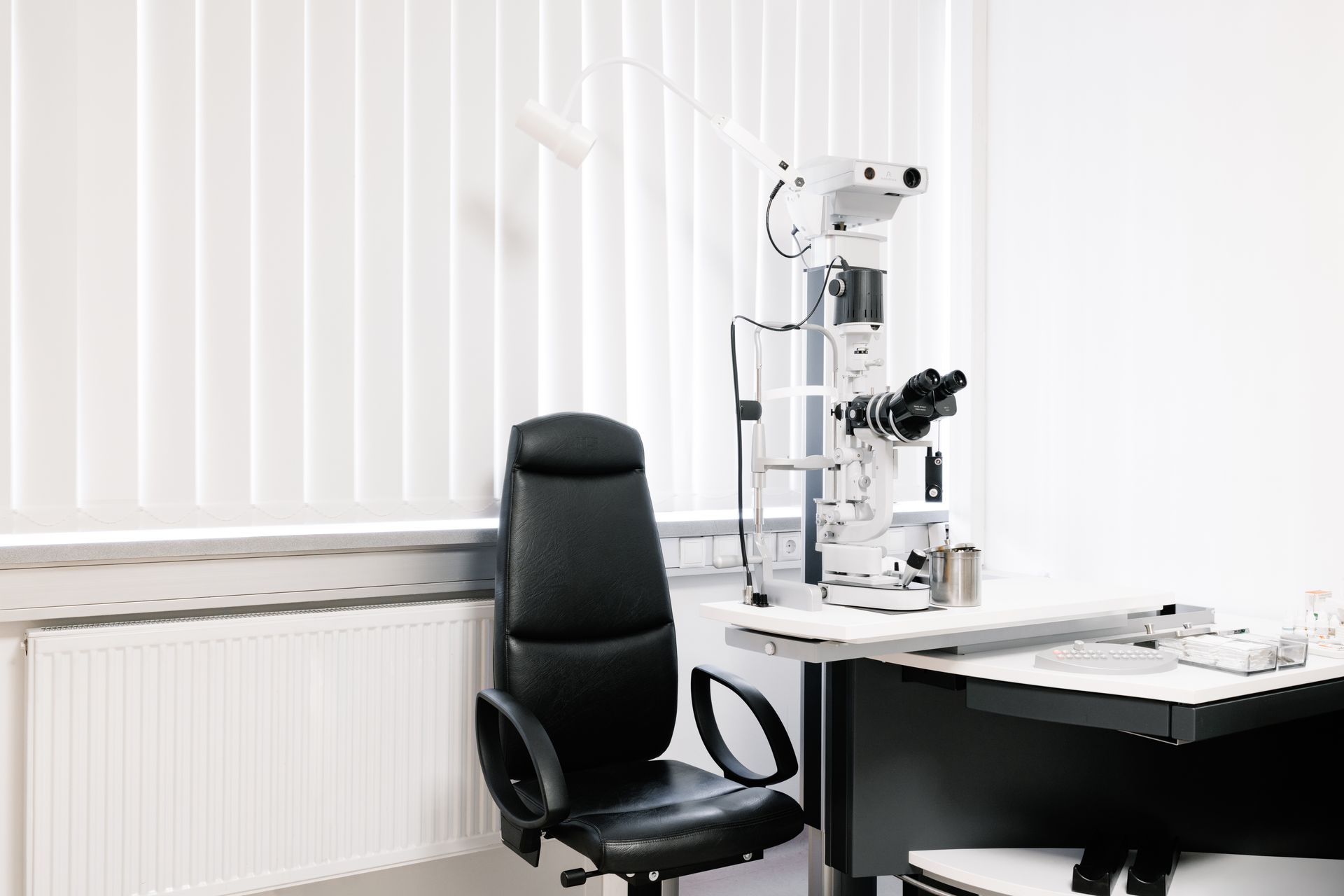 Ein Augenuntersuchungsraum mit einem schwarzen Ledersessel vor einem Spaltlampenmikroskop auf einem weißen Schreibtisch.
