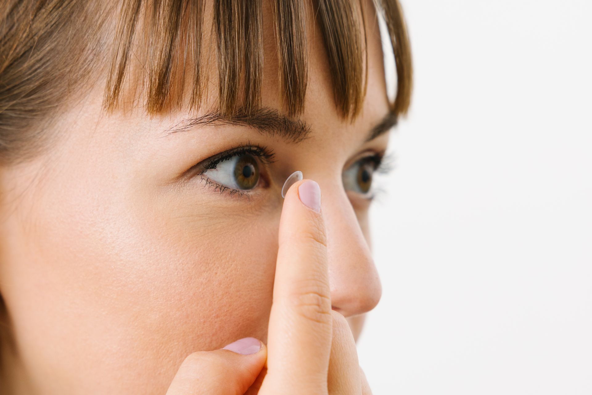 Eine Person setzt sich mit der Fingerspitze vorsichtig eine Kontaktlinse aufs Auge, vor einem weißen Hintergrund.