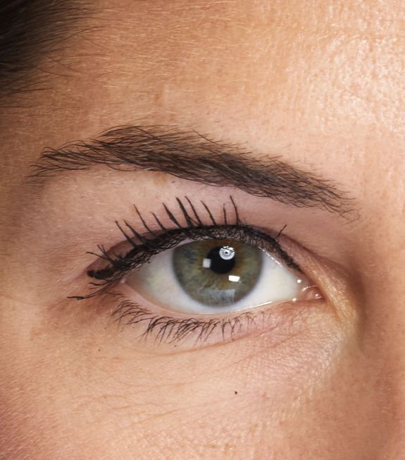 Nahaufnahme eines grünen Auges mit dunkler Wimperntusche, Eyeliner und sorgfältig geformten Augenbrauen.
