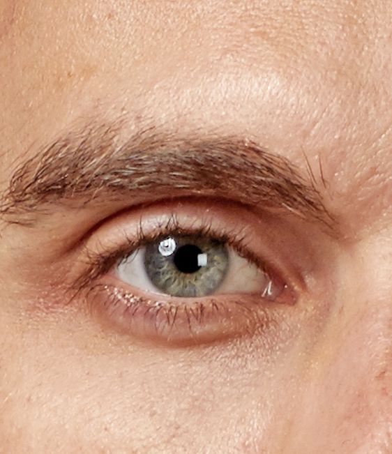 Nahaufnahme eines menschlichen Auges mit graugrüner Iris und heller Haut, Fokus auf Auge und Augenbraue.