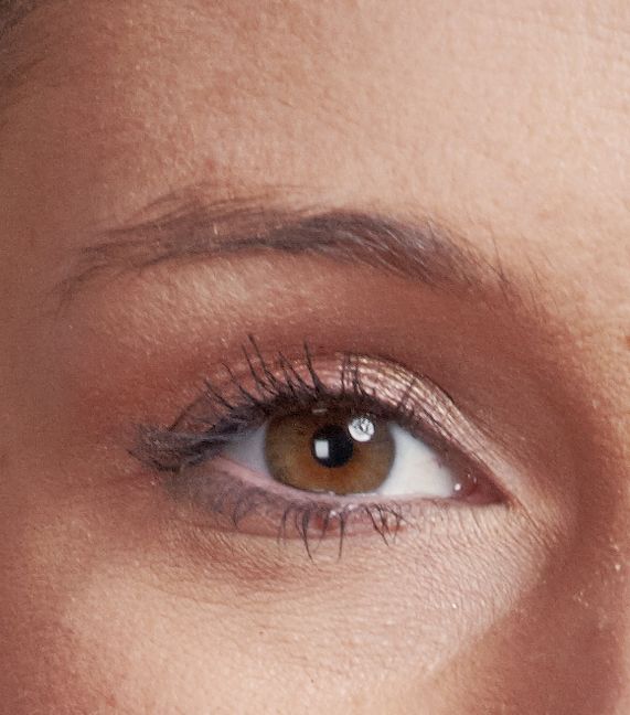 Nahaufnahme eines menschlichen Auges mit haselnussbrauner Iris, das dezentes Make-up und leichte Wimperntusche trägt.