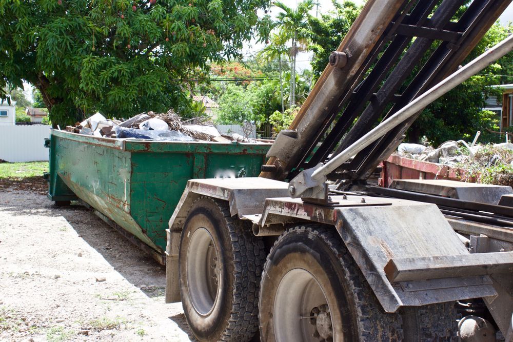 A green dumpster is sitting next to a dump truck.