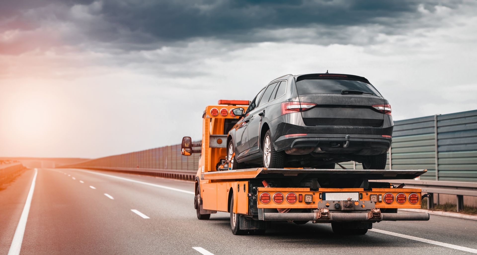 A tow truck is towing a car on a highway.