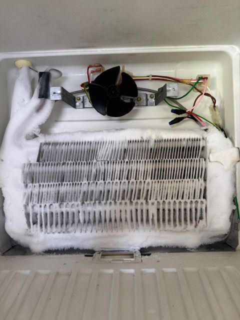 The inside of a refrigerator with a fan and wires.