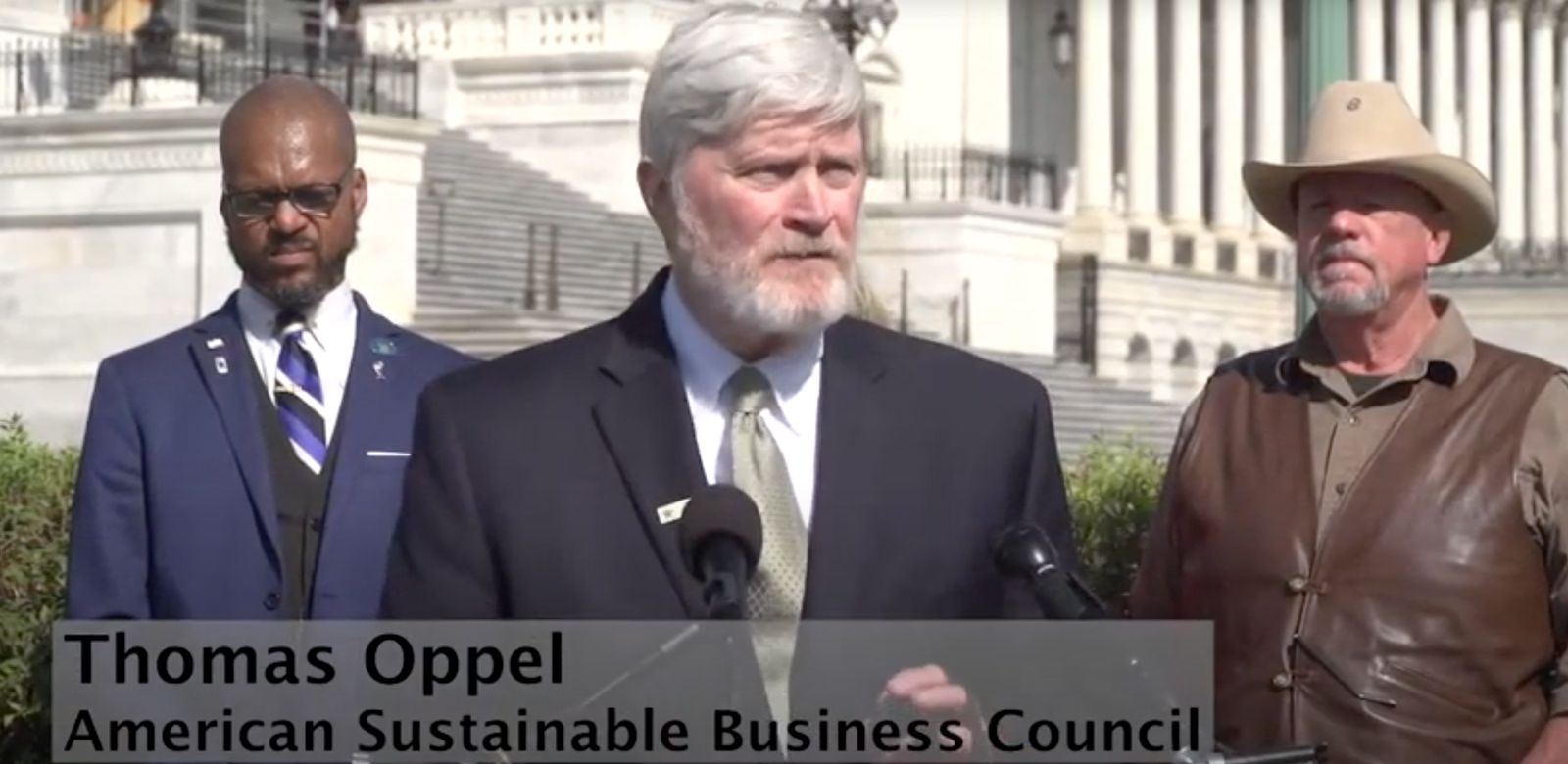 Thomas Oppel in a suit and tie is standing in front of a microphone for the American Sustainable Business Council