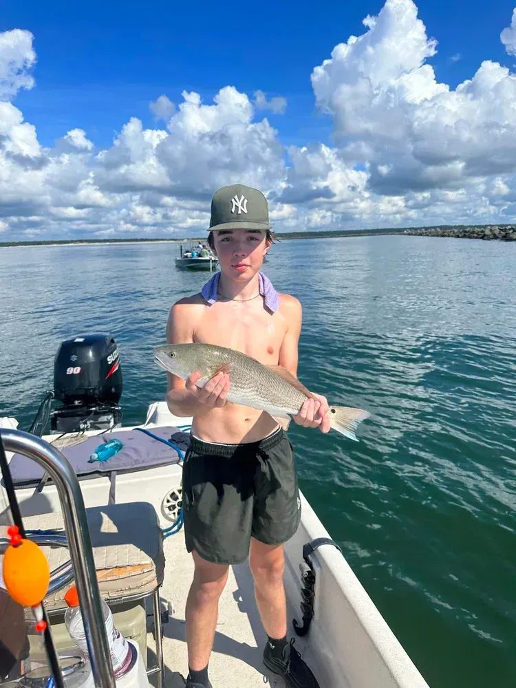 Teenager on a boat holding a fish, sunny day, blue sky with clouds.