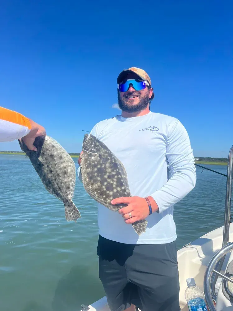 Man on boat holds two speckled fish; blue sky and water background.