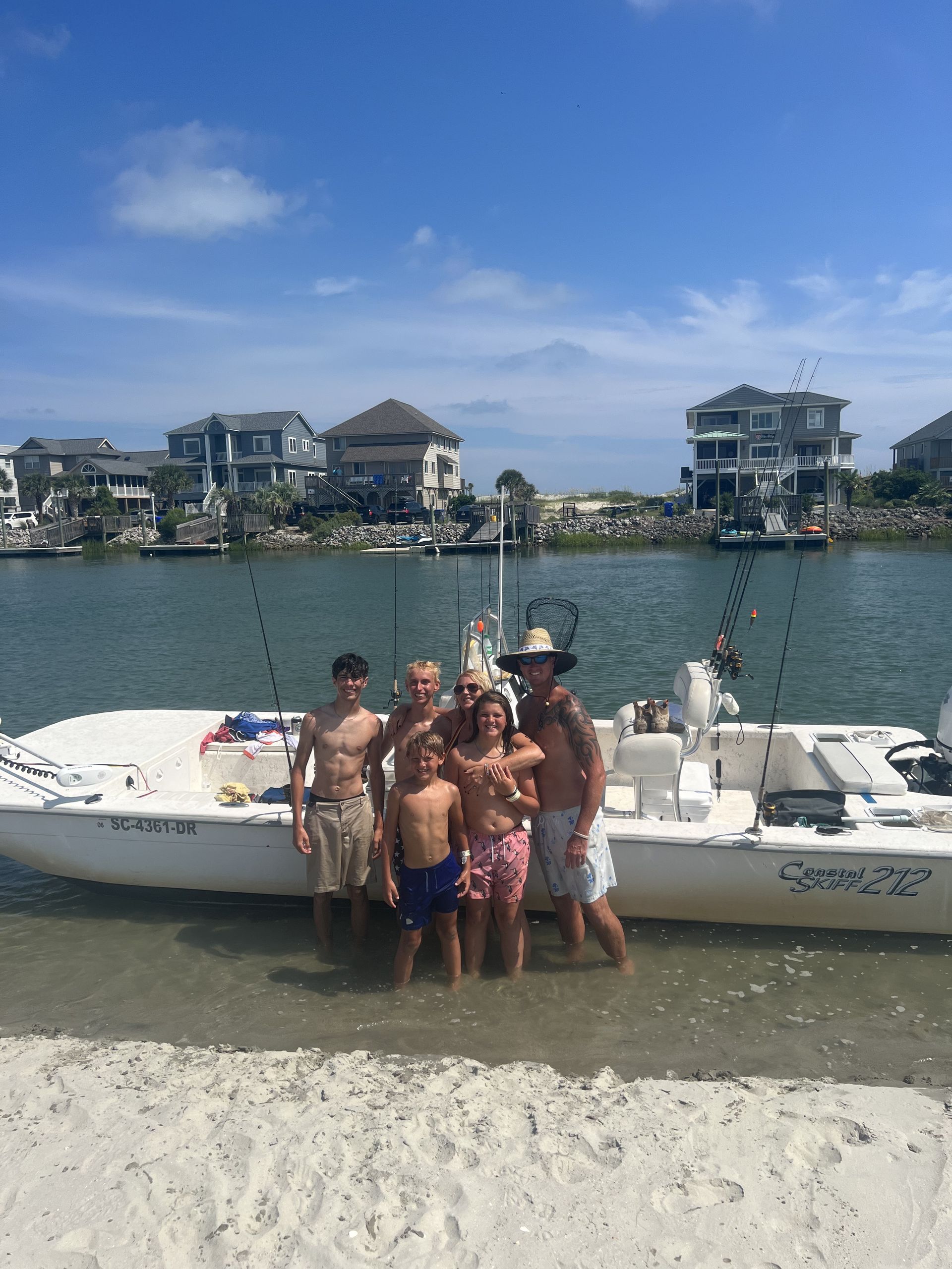 Man on boat, reeling in a large, white stingray. Blue water, clear sky. He is shirtless, smiling, fist raised.