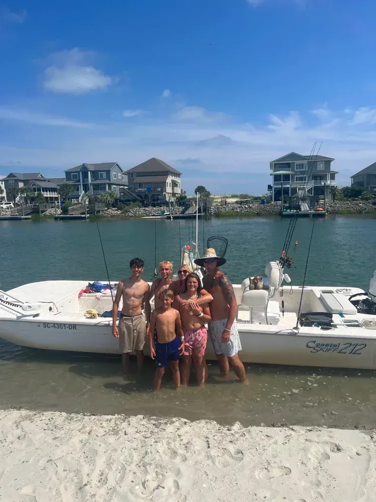 Family posing on a beach by a boat on a sunny day. Houses in the background.