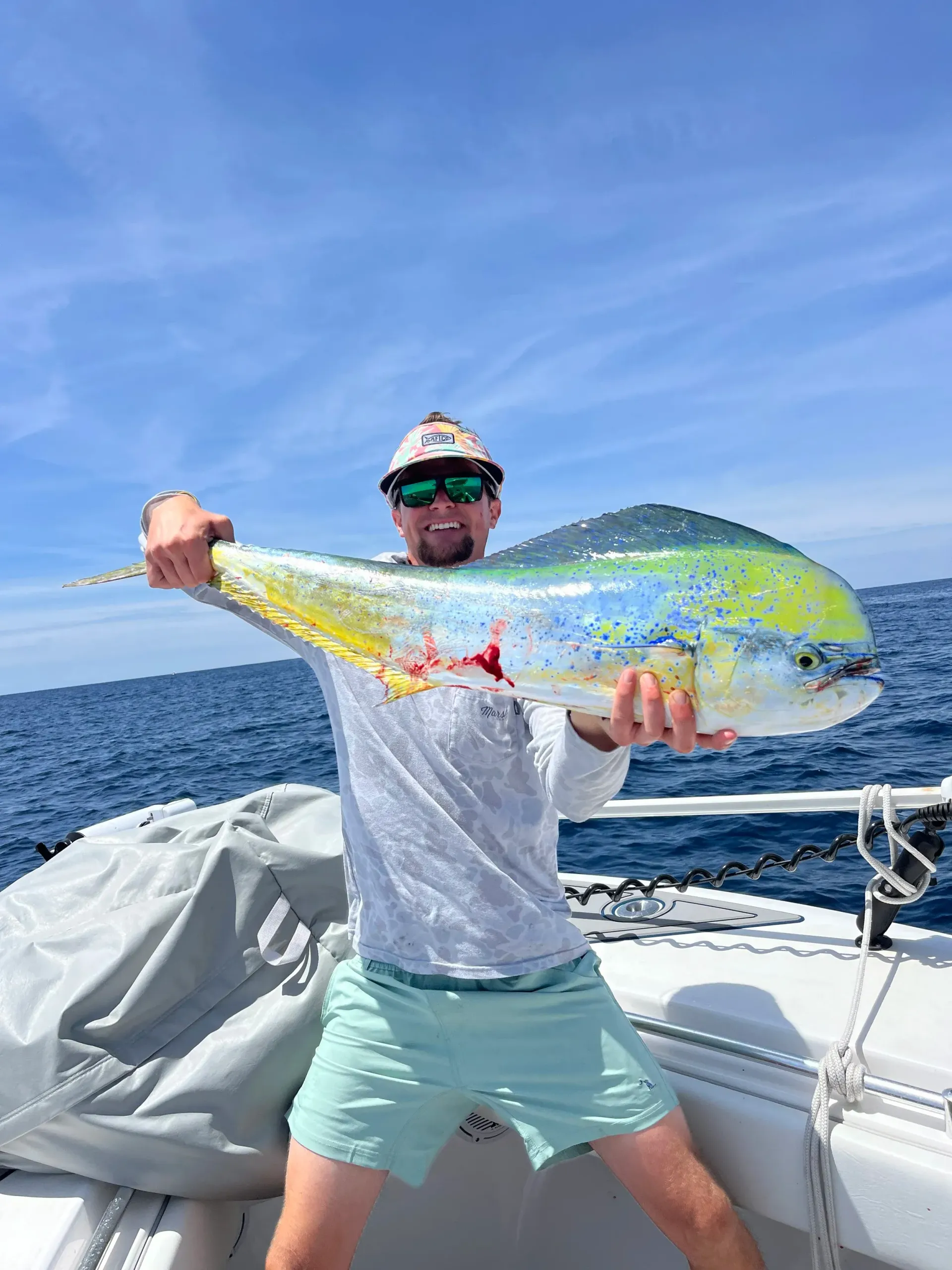Man on boat holding up large, colorful Mahi-Mahi fish against a blue sky and ocean.