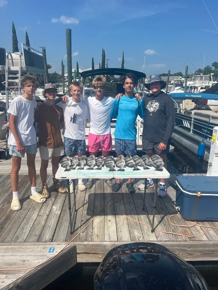 Six people pose with a table of fish on a dock, sunny day.