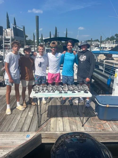 Six people pose with a table of fish on a dock, sunny day.