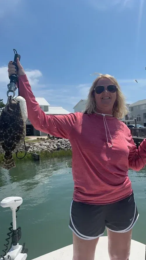 Woman on boat holds up fish she caught on a sunny day.