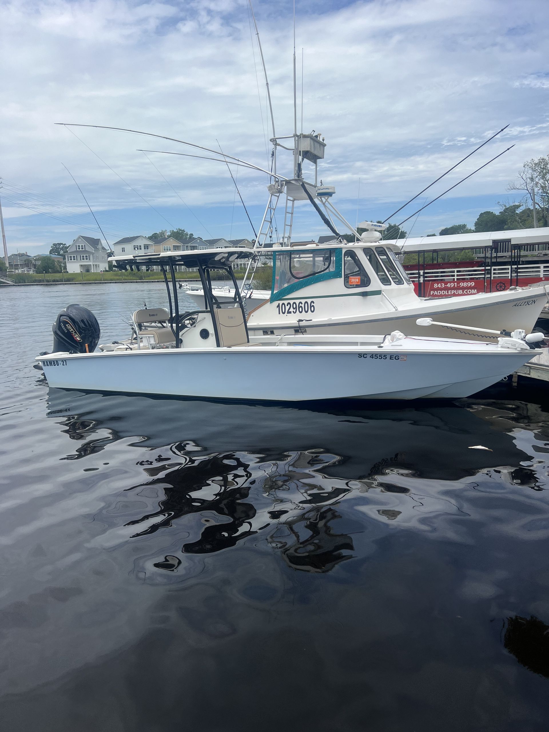 White fishing boat beached on a sandy shore, connected by a line to an anchor in the sand. Overcast sky.
