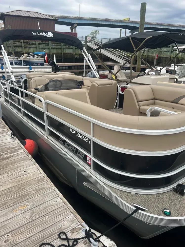 A pontoon boat docked at a pier with tan seating and a black canopy.