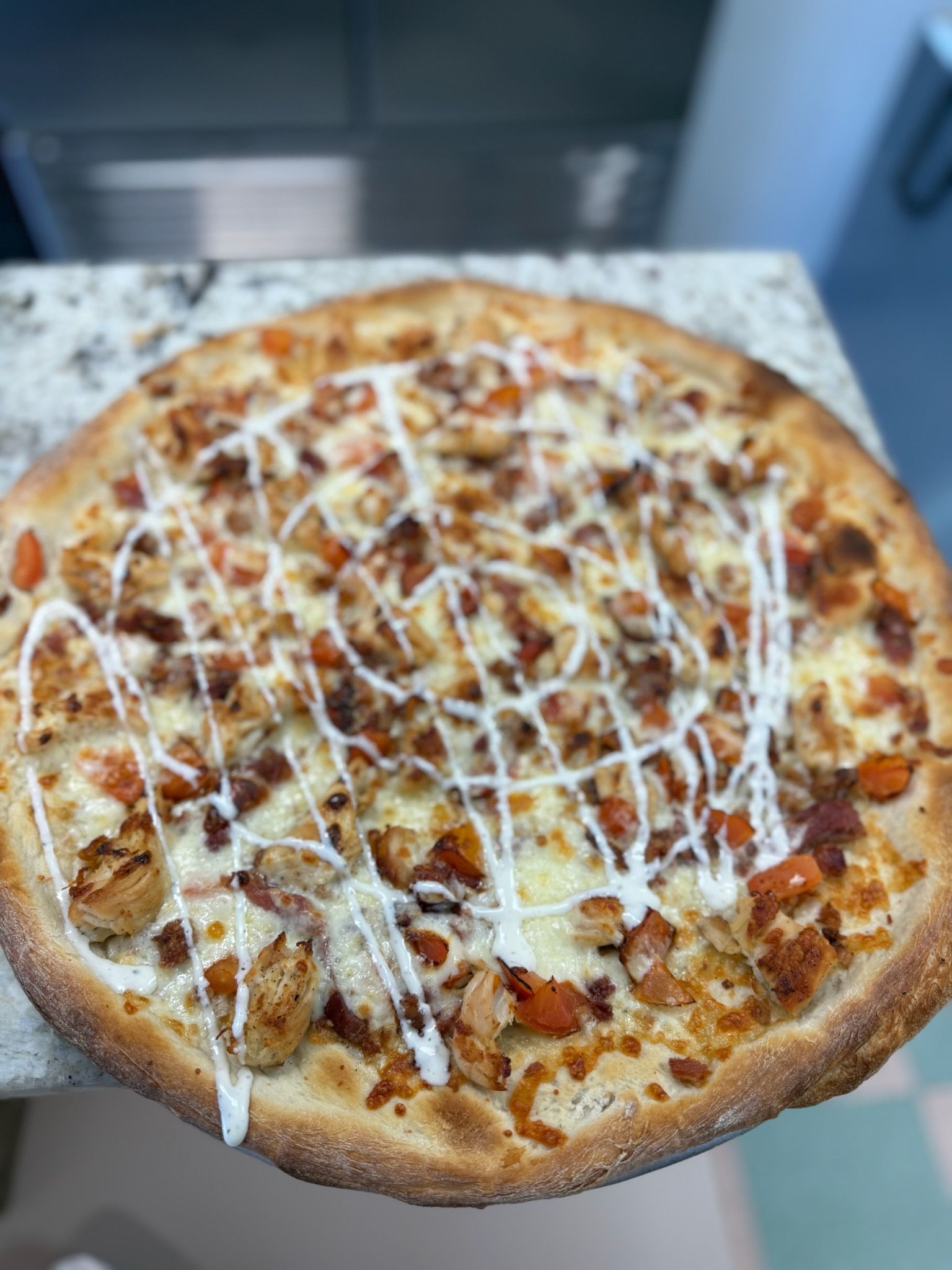 Cheese pizza topped with white drizzle on a granite countertop