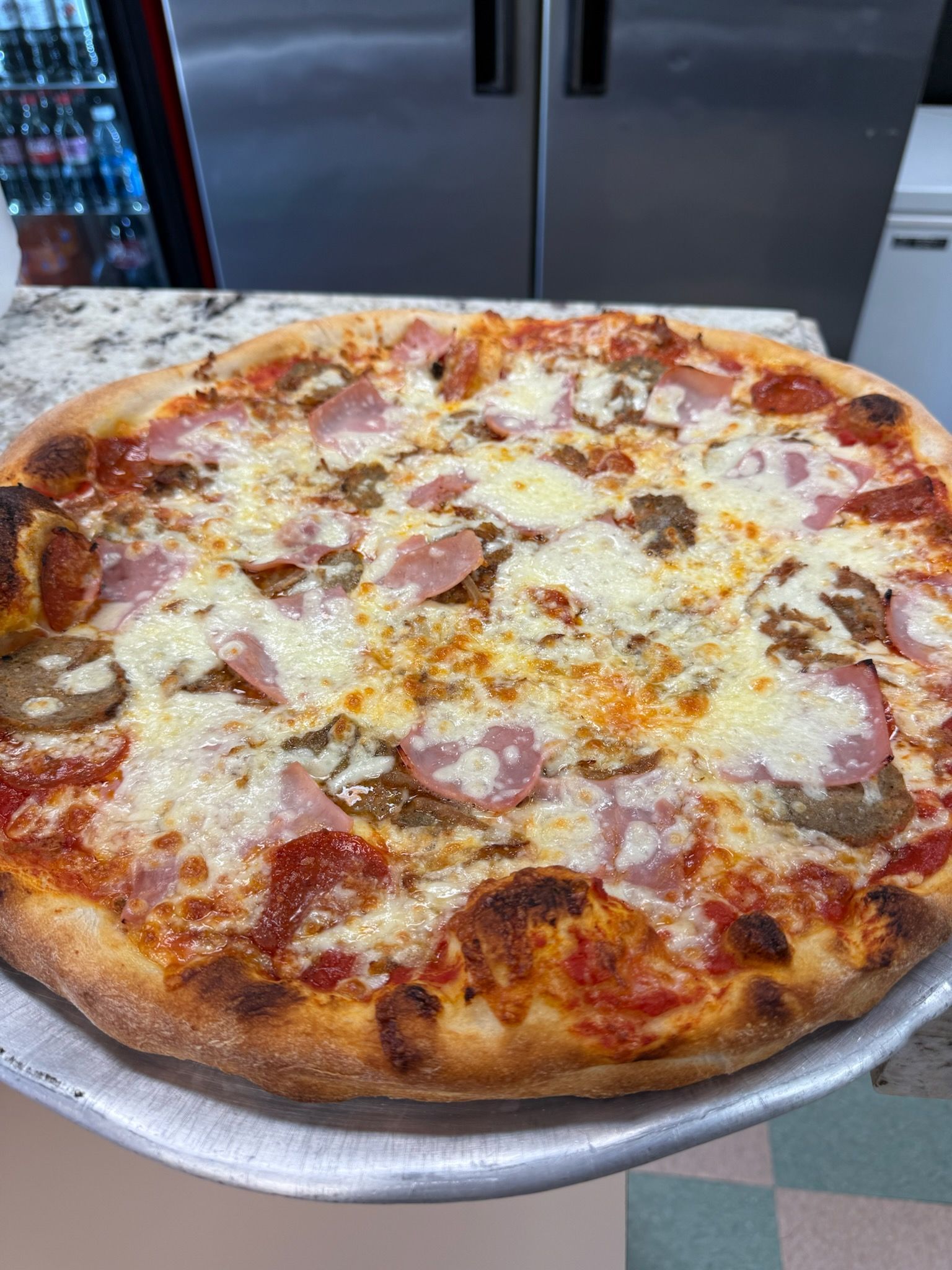 Large pepperoni and cheese pizza on a metal tray in a kitchen