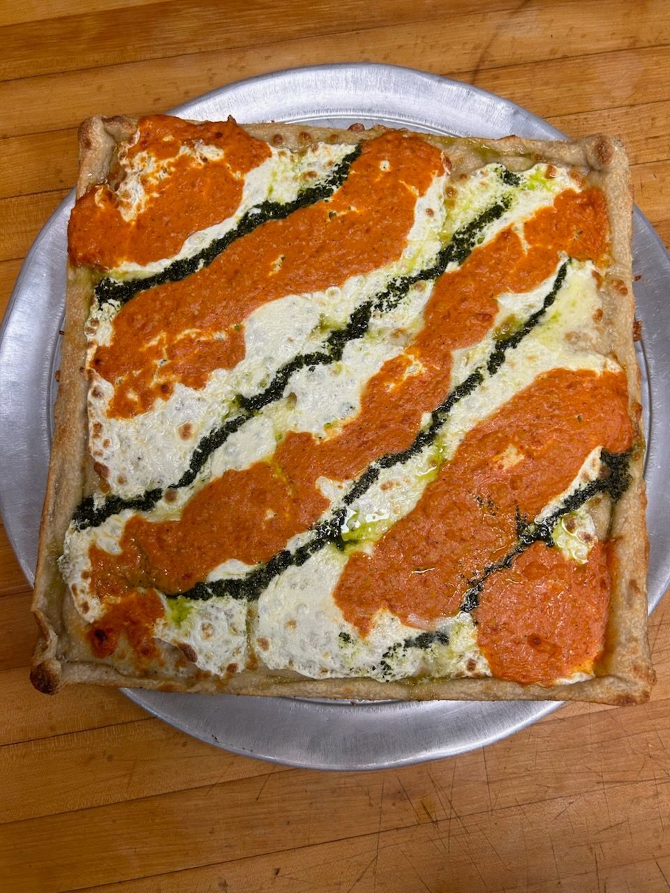 Square slice of pizza with orange and white topping on a white plate