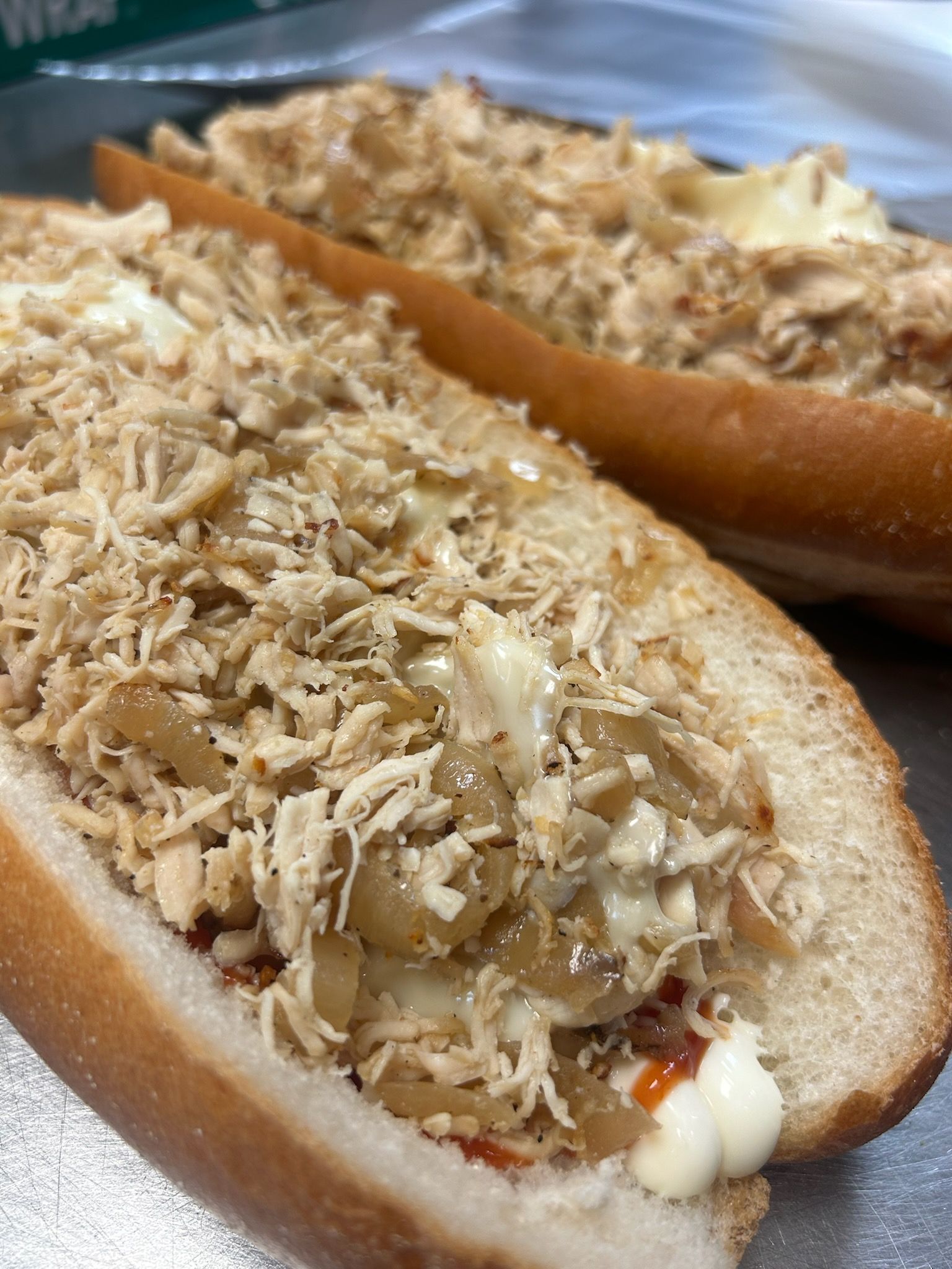 Two shredded-chicken sandwiches on white rolls, topped with creamy sauce