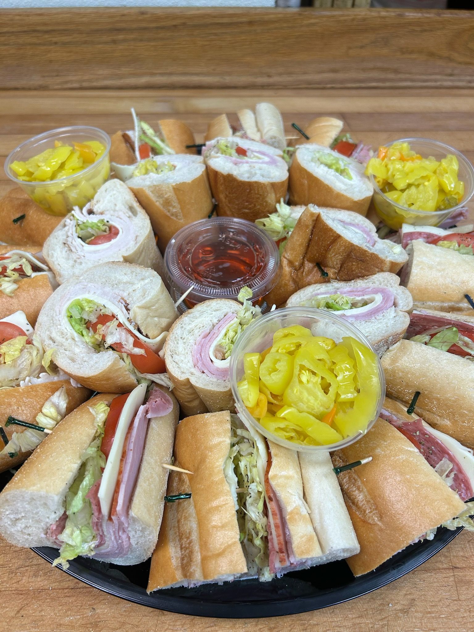 Assorted finger sandwiches and wraps arranged on a platter with dips and yellow pickles