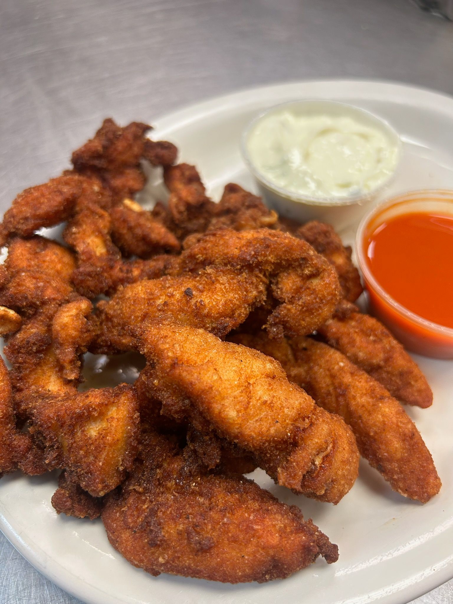 Plate of fried chicken wings with white dipping sauce and orange sauce on a table