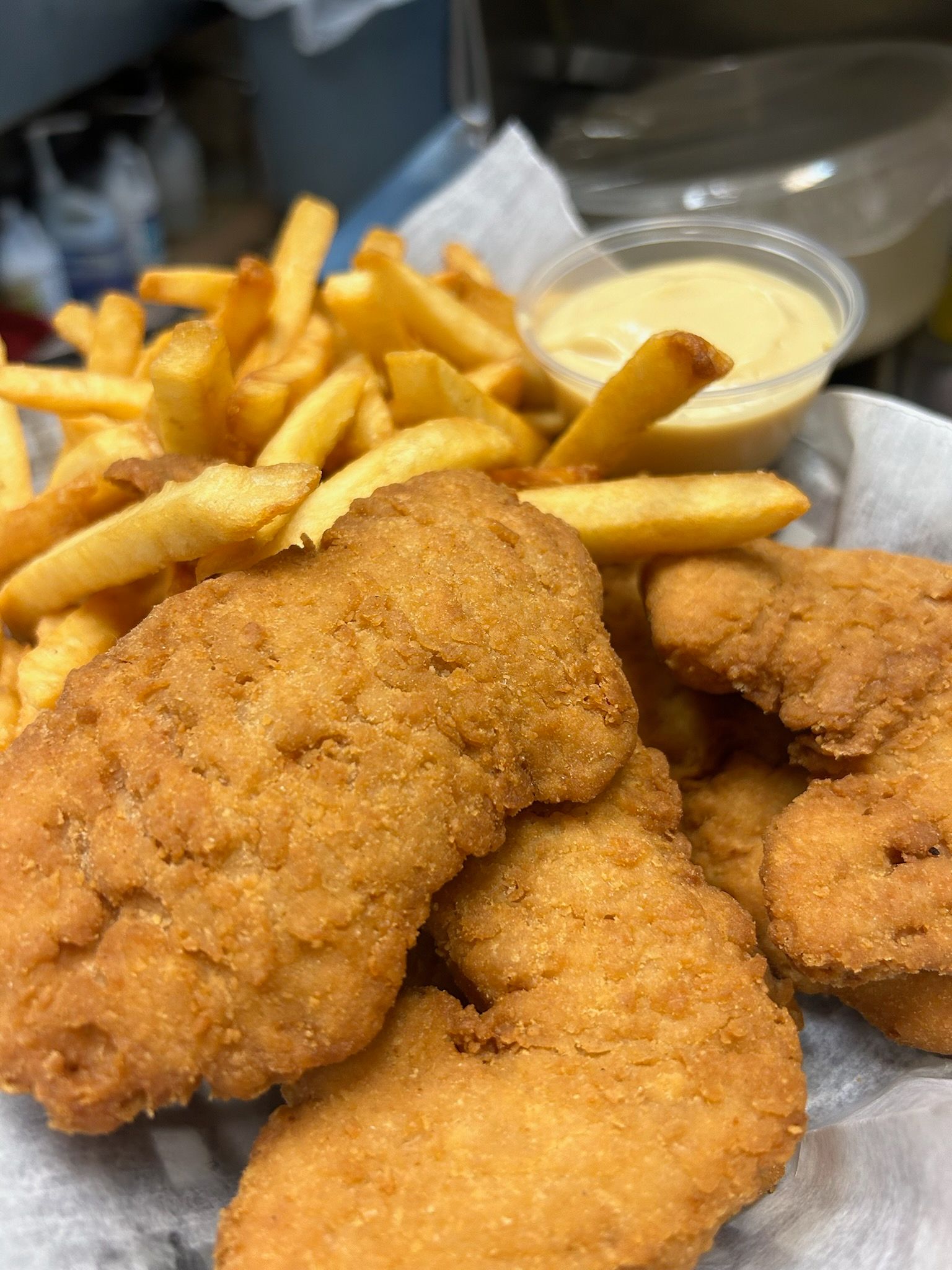 Fried chicken tenders with French fries and a cup of dipping sauce on a tray