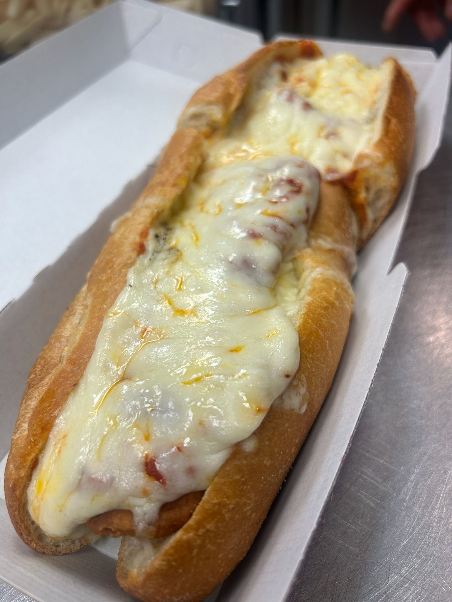 Cheesy Italian sandwich on a white tray, with melted mozzarella and marinara in a toasted roll