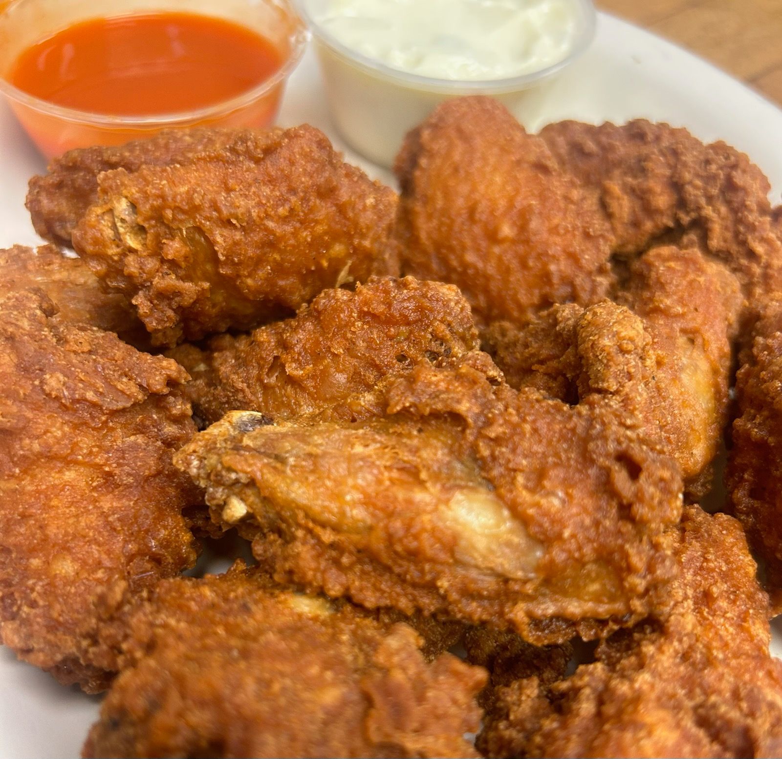 Plate of crispy fried chicken wings with orange and white dipping sauces in the background