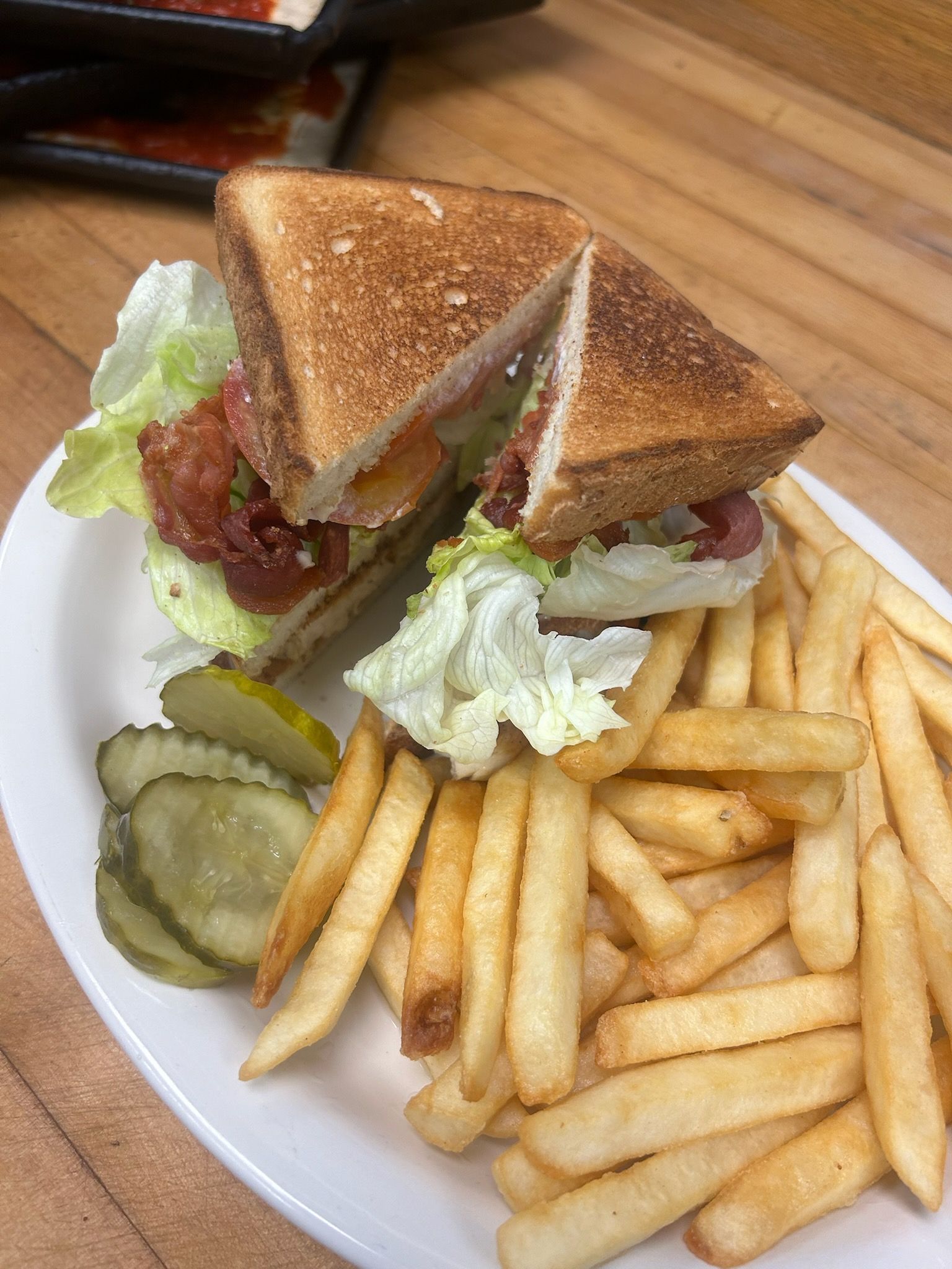 Grilled sandwich with lettuce, pickles, and fries on a white plate on a wooden table