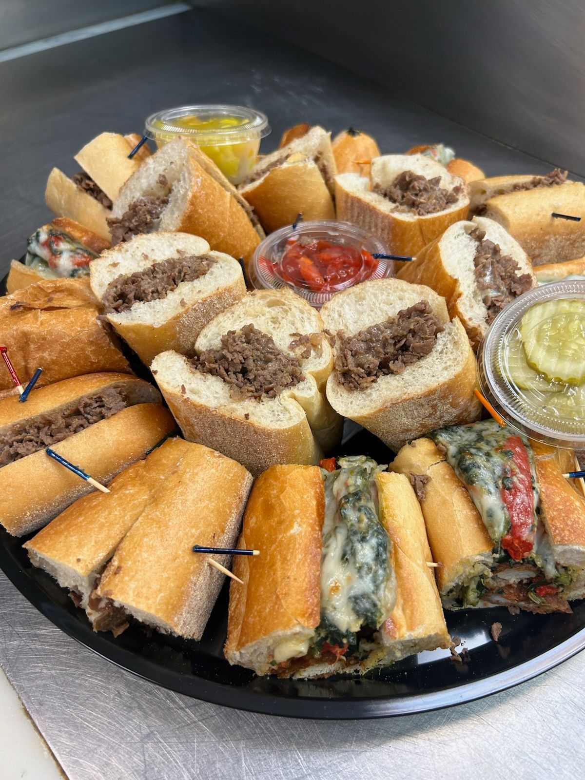 Assorted tea sandwiches and savory rolls arranged on a black platter with dipping sauces