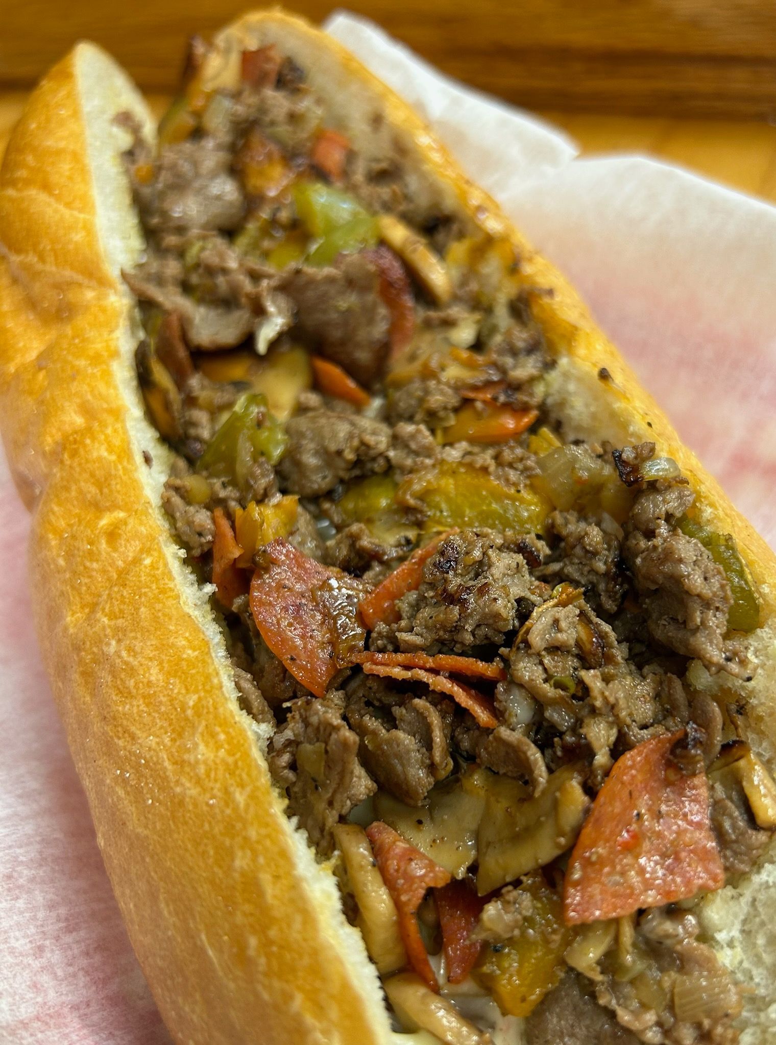 Loaded sandwich on a baguette with chopped meat and peppers on paper, close-up view