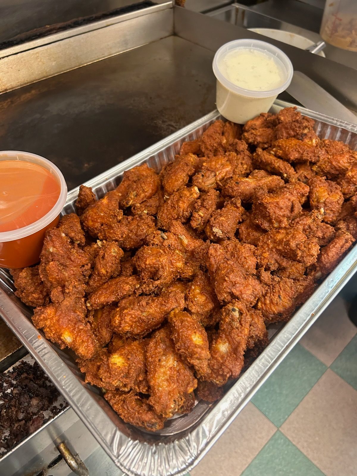 Tray of sauced chicken wings with two dipping cups on a buffet counter