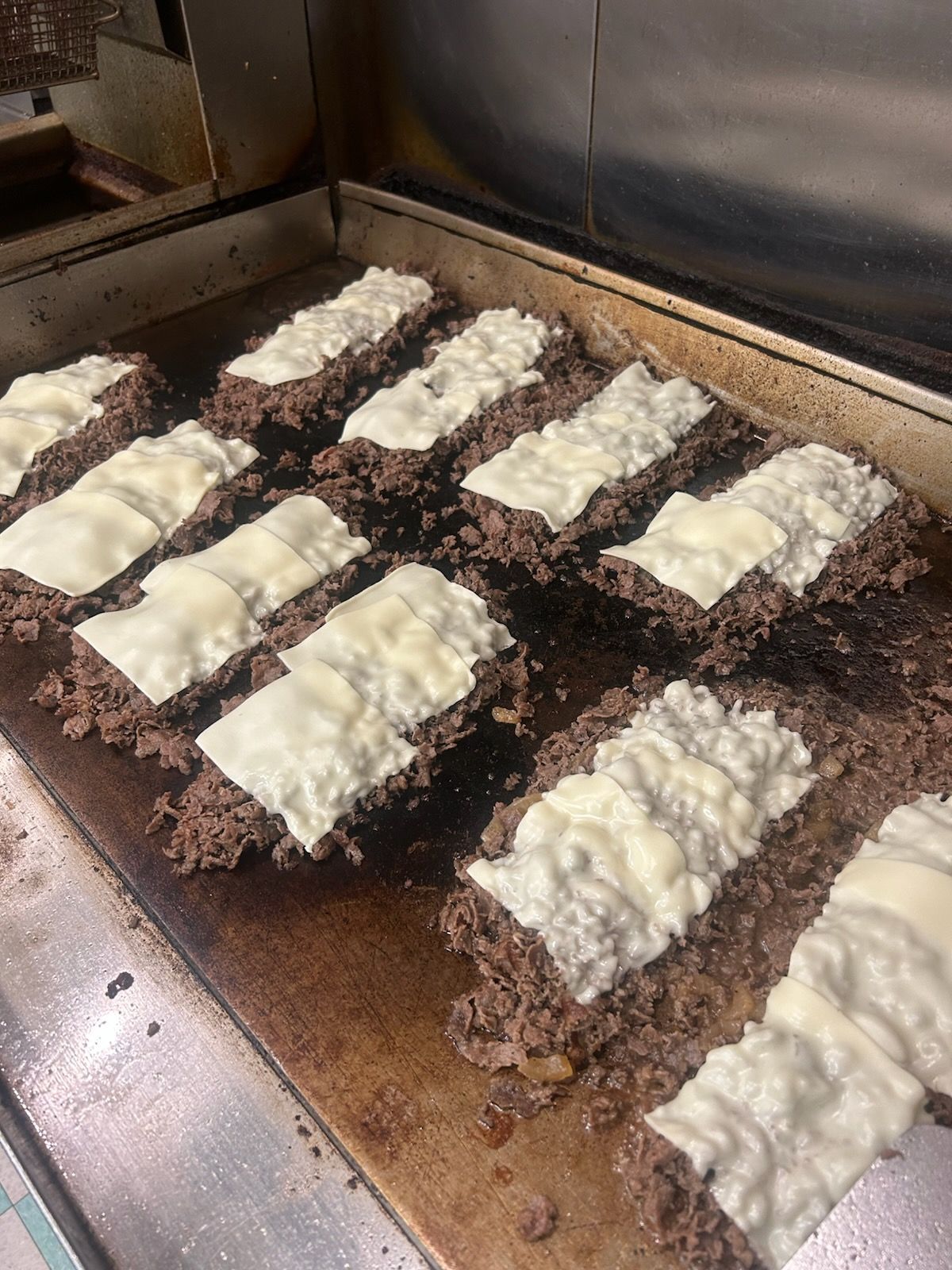 Breaded meat strips topped with melted white cheese cooking on a grill.