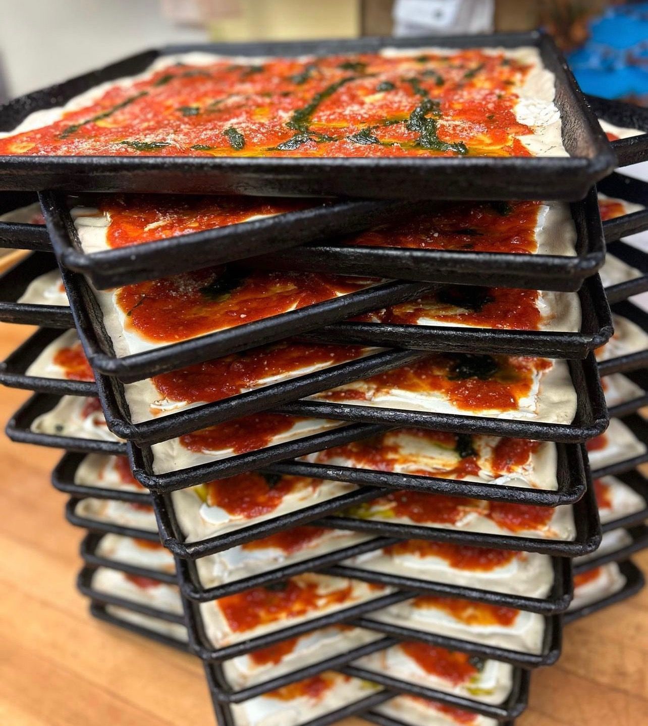 Stack of black trays holding red-orange sauced food on a countertop.