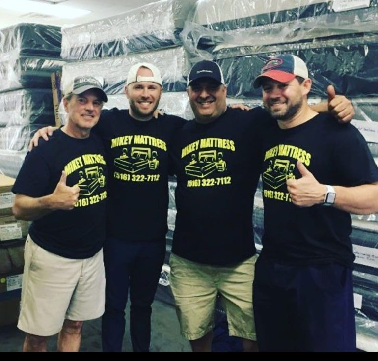 four men wearing mikey mattress shirts pose for a photo
