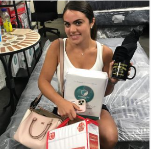 a woman is sitting on a bed holding a purse and a mikey mattress mug