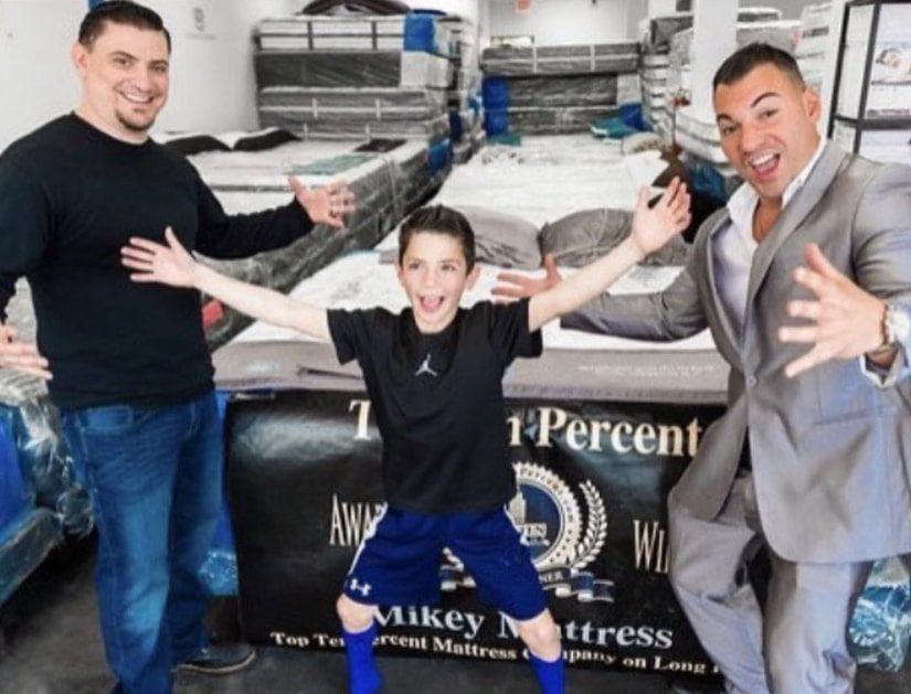 a boy stands in front of a sign that says mikey mattress