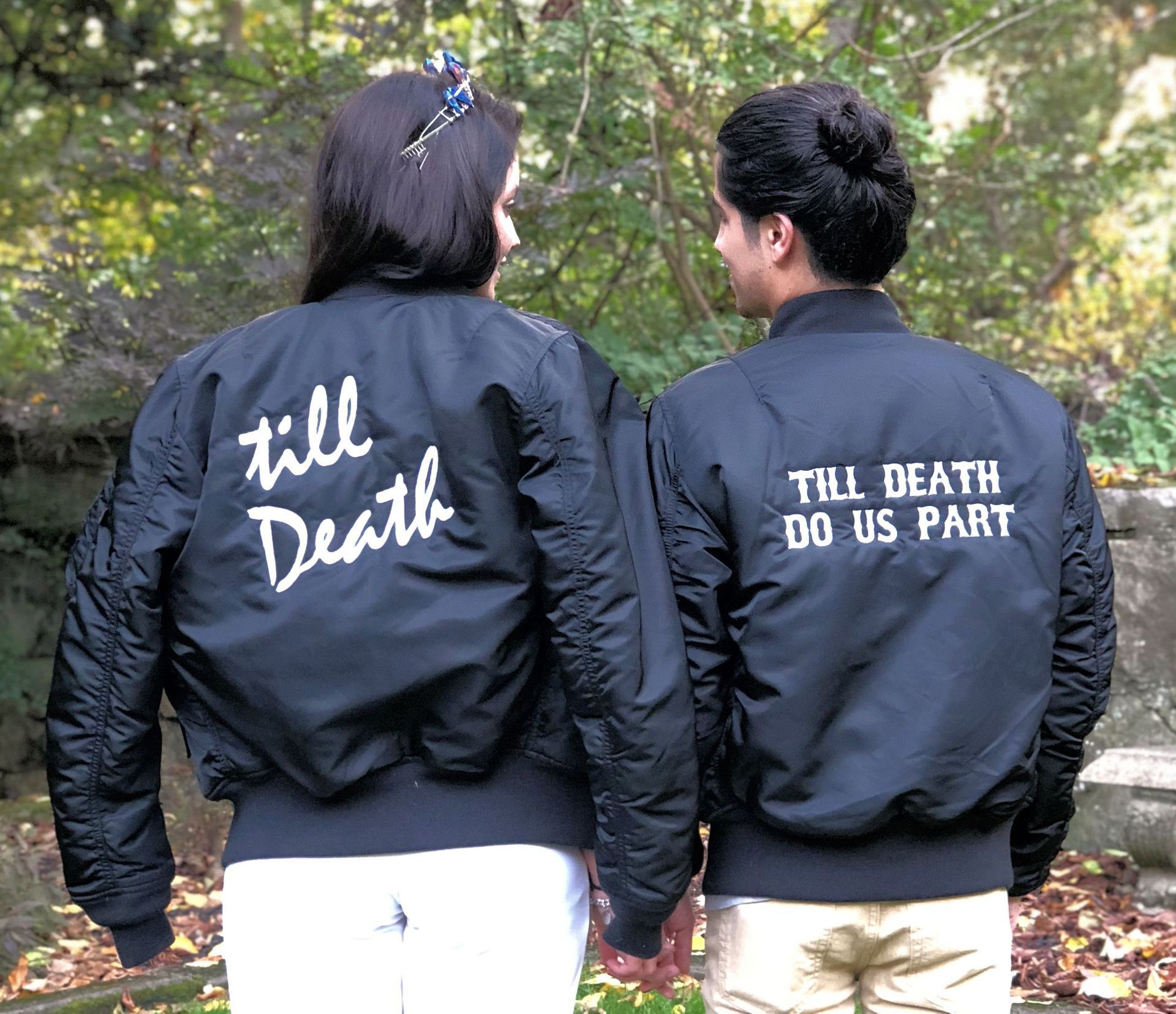 Two people wearing black bomber jackets with white text on the back: 