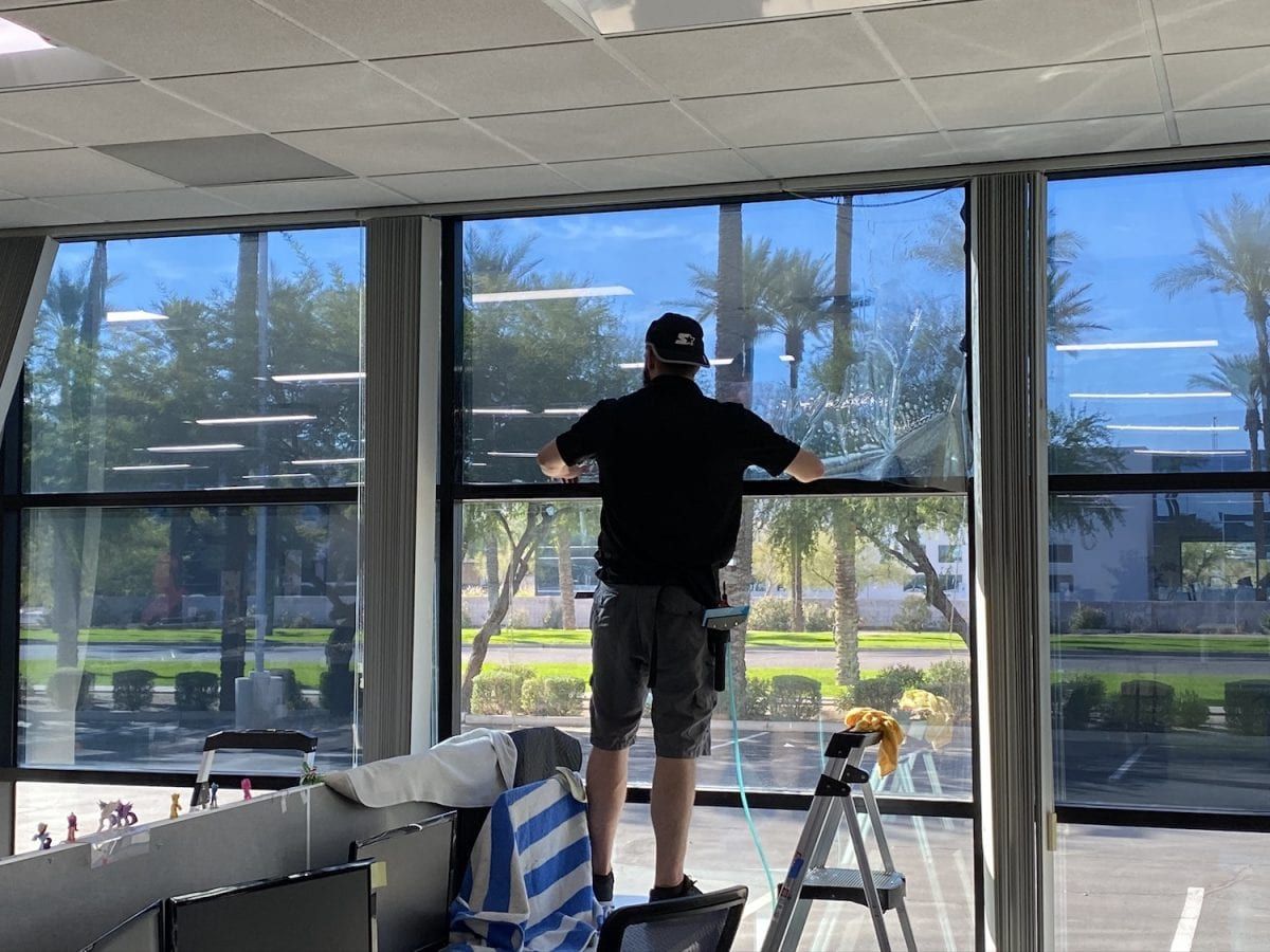 a man standing on a ladder installing tint on a window