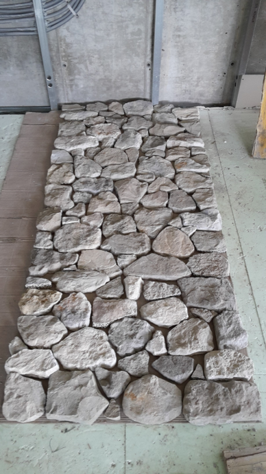 Una sezione rettangolare di rivestimento murale in pietra grigia, caratterizzata da un assortimento di pezzi di roccia irregolari dall'aspetto naturale.